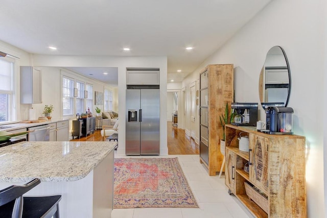 kitchen with white cabinets, stainless steel appliances, light stone counters, and light hardwood / wood-style floors