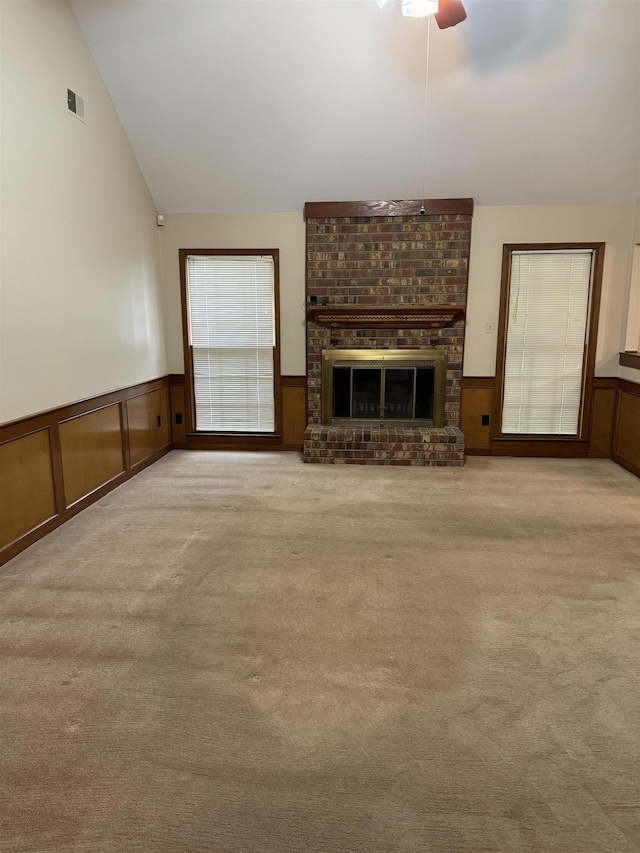 unfurnished living room with a brick fireplace, light colored carpet, vaulted ceiling, ceiling fan, and wood walls