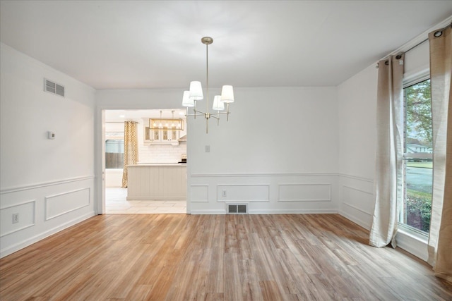 spare room featuring a notable chandelier and light hardwood / wood-style flooring