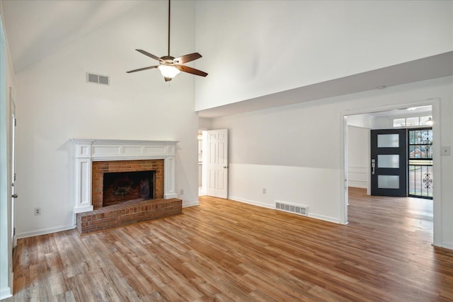 unfurnished living room with hardwood / wood-style floors, high vaulted ceiling, ceiling fan, and a brick fireplace