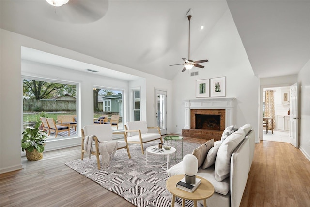 living room with ceiling fan, light wood-type flooring, a fireplace, and high vaulted ceiling