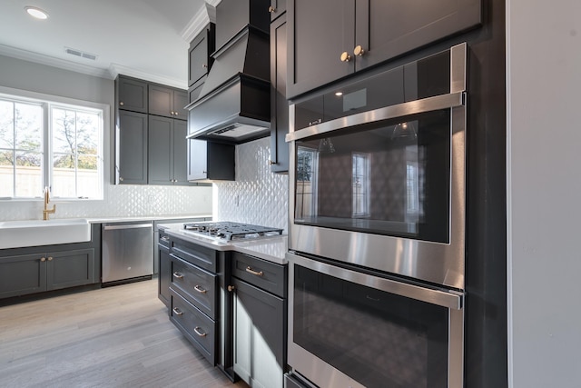 kitchen featuring decorative backsplash, appliances with stainless steel finishes, ornamental molding, sink, and light hardwood / wood-style flooring