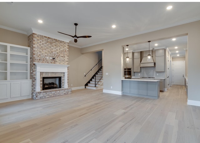 unfurnished living room featuring ceiling fan, light wood-type flooring, ornamental molding, and a fireplace