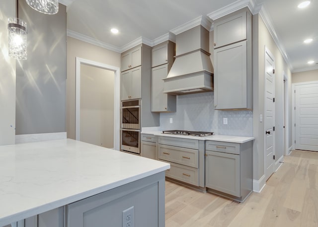 kitchen featuring custom range hood, light wood-type flooring, decorative light fixtures, and backsplash