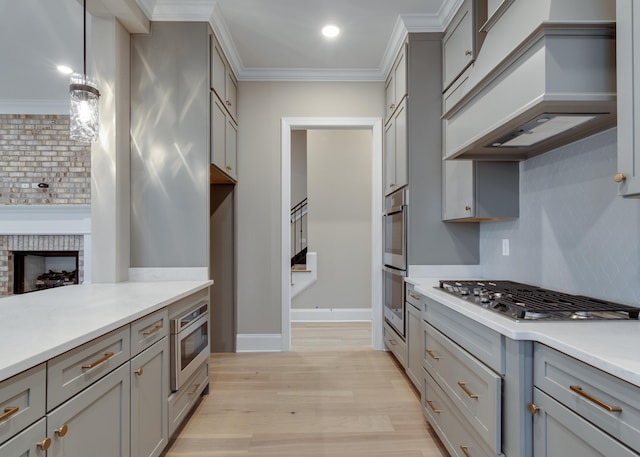 kitchen with appliances with stainless steel finishes, tasteful backsplash, premium range hood, gray cabinetry, and decorative light fixtures