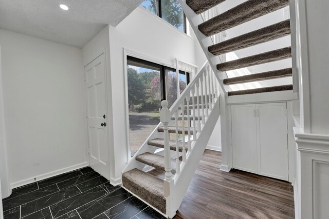 staircase with a textured ceiling, hardwood / wood-style floors, and lofted ceiling