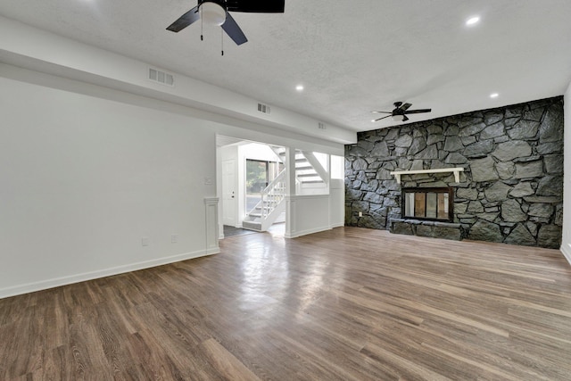 unfurnished living room with wood-type flooring, a textured ceiling, a stone fireplace, and ceiling fan