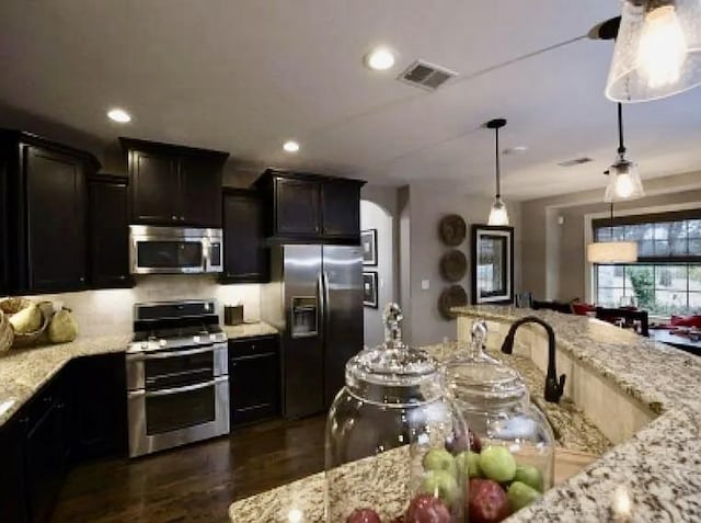 kitchen with stainless steel appliances, light stone counters, dark hardwood / wood-style floors, pendant lighting, and dark brown cabinets