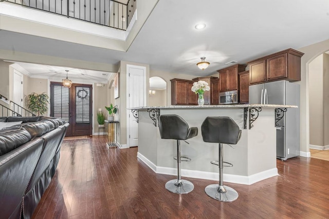 kitchen with hanging light fixtures, stainless steel appliances, dark hardwood / wood-style flooring, a breakfast bar, and ornamental molding