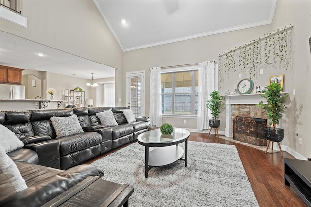 living room with dark wood-type flooring, high vaulted ceiling, a notable chandelier, a fireplace, and ornamental molding