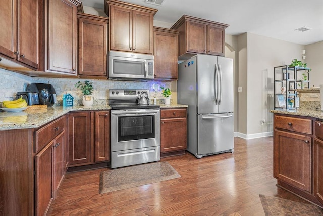 kitchen featuring light stone countertops, stainless steel appliances, tasteful backsplash, and dark wood-type flooring