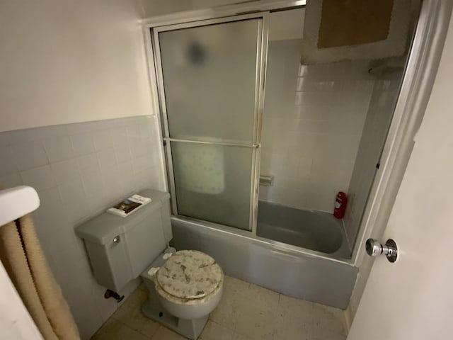 bathroom featuring toilet, tile patterned floors, tile walls, and bath / shower combo with glass door