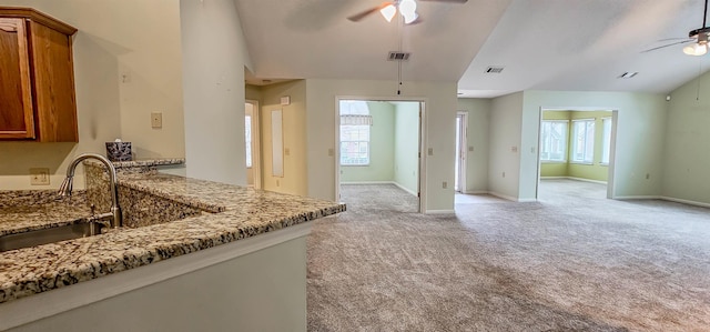 kitchen featuring ceiling fan, vaulted ceiling, a wealth of natural light, and dark stone countertops