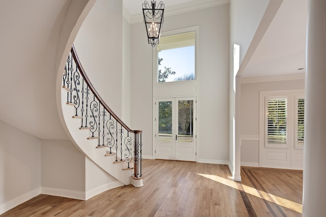 entryway with french doors, light wood-type flooring, ornamental molding, a towering ceiling, and a chandelier