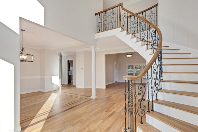 staircase featuring hardwood / wood-style floors, decorative columns, an inviting chandelier, and ornamental molding