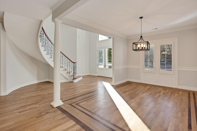 entryway with light hardwood / wood-style floors, an inviting chandelier, decorative columns, and crown molding