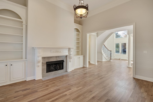 unfurnished living room featuring built in shelves, french doors, crown molding, light hardwood / wood-style floors, and a fireplace