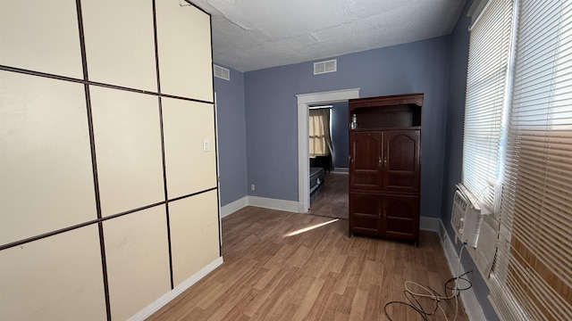 unfurnished bedroom featuring a textured ceiling, light hardwood / wood-style floors, and a wall mounted AC