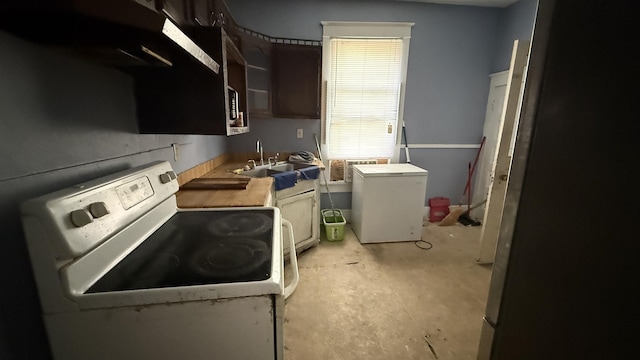 kitchen featuring white range oven, dark brown cabinetry, sink, and refrigerator