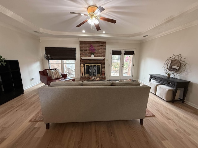 unfurnished living room with light wood-type flooring, a brick fireplace, ornamental molding, a raised ceiling, and ceiling fan