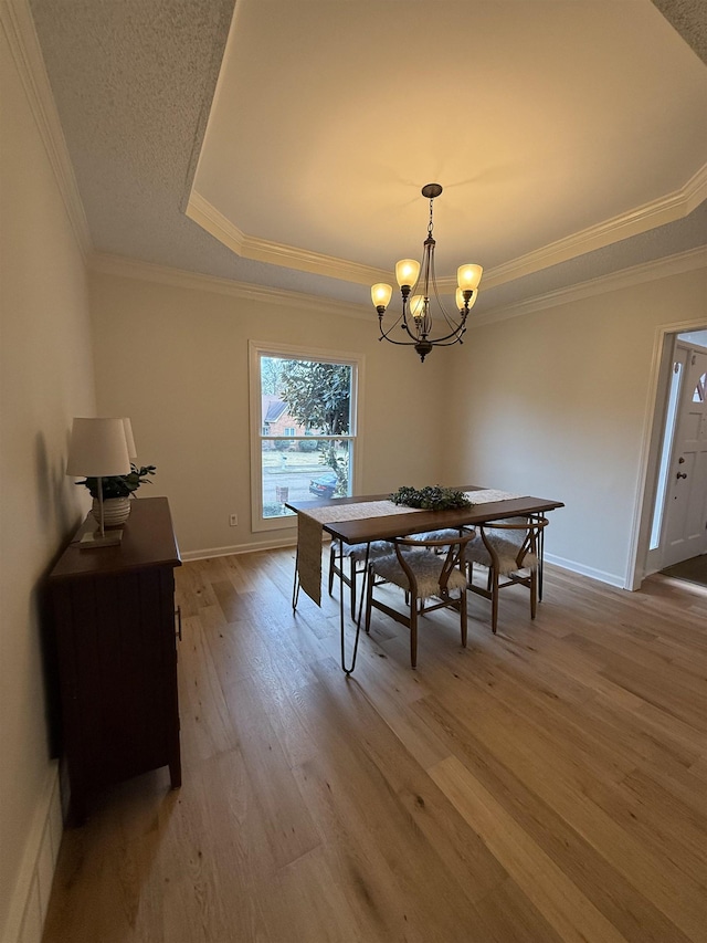 dining space featuring a tray ceiling, ornamental molding, light hardwood / wood-style floors, and a notable chandelier