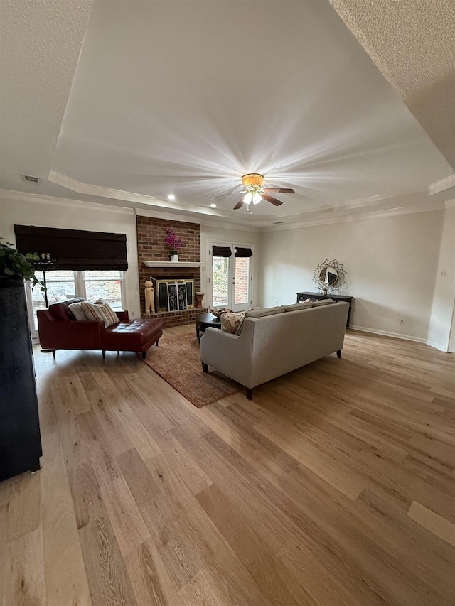 living room with a raised ceiling, a fireplace, crown molding, and light hardwood / wood-style flooring