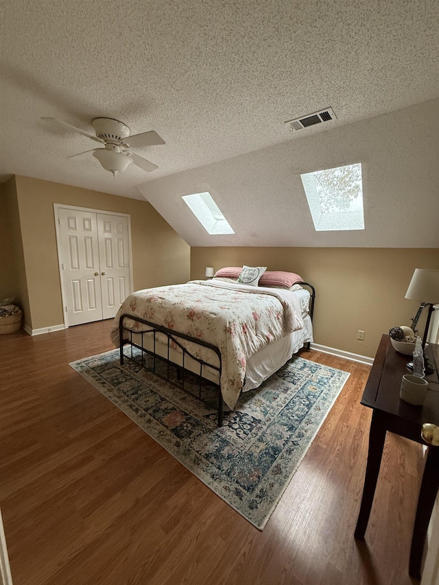 bedroom with lofted ceiling with skylight, hardwood / wood-style flooring, ceiling fan, a textured ceiling, and a closet