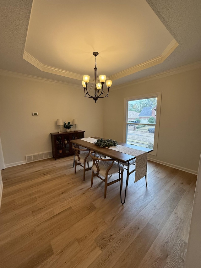 dining space with a tray ceiling, hardwood / wood-style floors, a chandelier, and ornamental molding