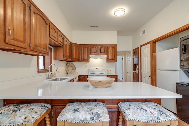 kitchen with kitchen peninsula, a breakfast bar, white appliances, and sink