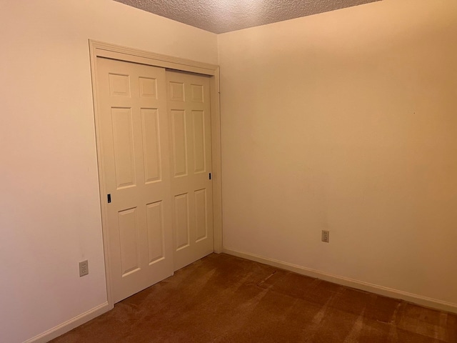 unfurnished bedroom featuring dark colored carpet, a textured ceiling, and a closet