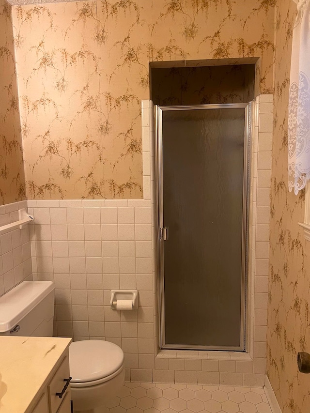 bathroom with tile patterned floors, vanity, tile walls, toilet, and a shower with shower door