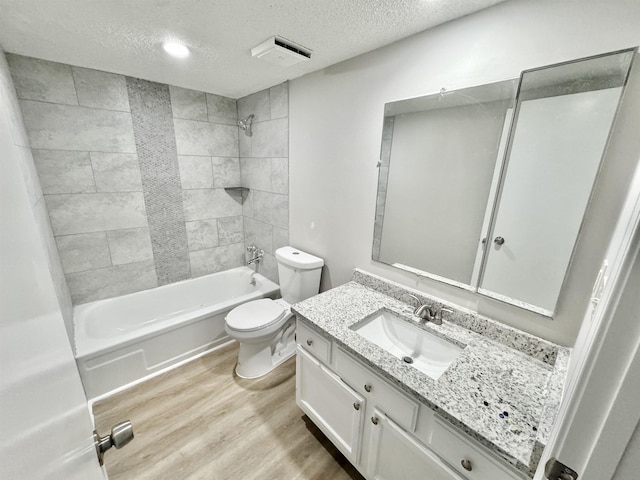 full bathroom featuring vanity, a textured ceiling, hardwood / wood-style floors, toilet, and tiled shower / bath