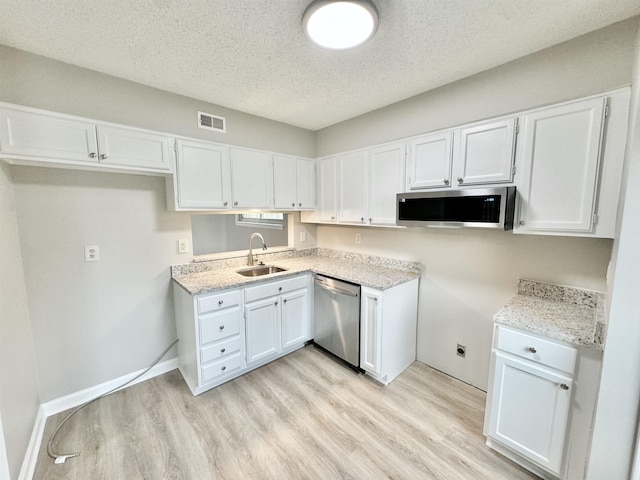 kitchen with appliances with stainless steel finishes, a textured ceiling, sink, light hardwood / wood-style floors, and white cabinetry