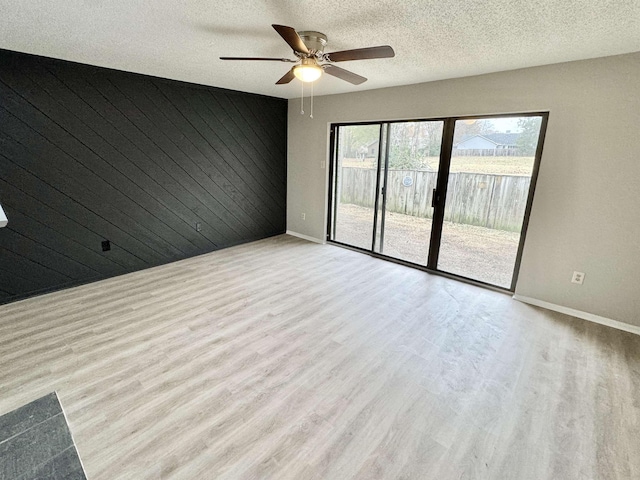 empty room with wood walls, a textured ceiling, and light wood-type flooring