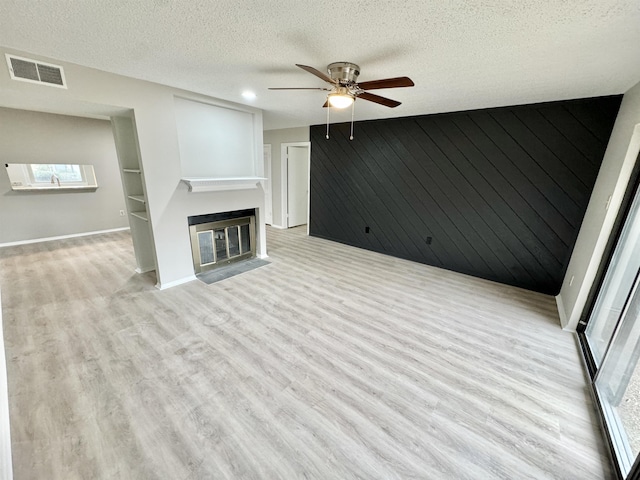 unfurnished living room featuring a textured ceiling, light hardwood / wood-style flooring, ceiling fan, and wood walls