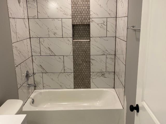 bathroom featuring toilet and tiled shower / bath