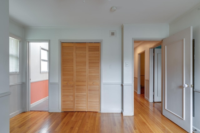 unfurnished bedroom featuring light hardwood / wood-style floors, ornamental molding, and a closet