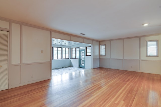 unfurnished living room featuring a healthy amount of sunlight, crown molding, and light hardwood / wood-style flooring