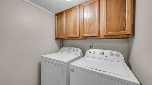 clothes washing area featuring washing machine and clothes dryer, cabinets, and a textured ceiling