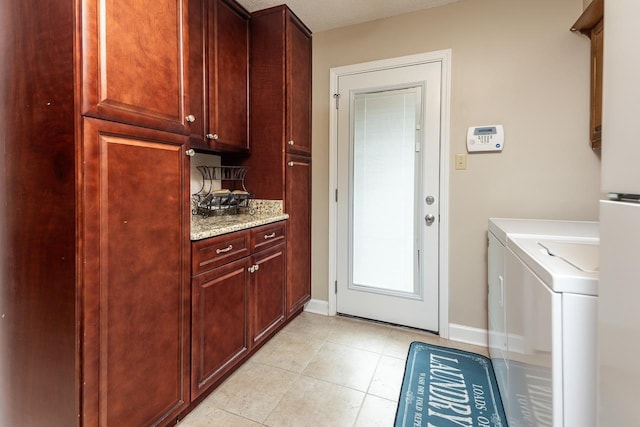 clothes washing area with washing machine and clothes dryer, light tile patterned floors, and cabinets