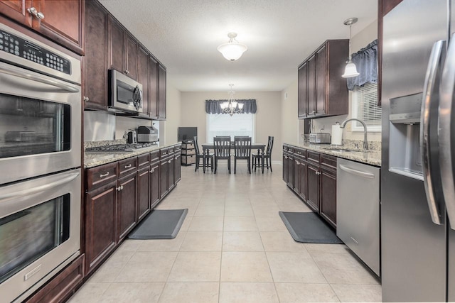 kitchen with light stone countertops, stainless steel appliances, sink, decorative light fixtures, and a chandelier