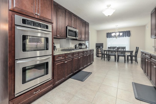 kitchen featuring hanging light fixtures, light tile patterned floors, light stone countertops, stainless steel appliances, and a chandelier