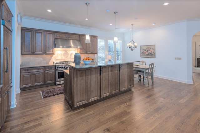 kitchen featuring light stone countertops, high end stove, dark wood-type flooring, pendant lighting, and an island with sink