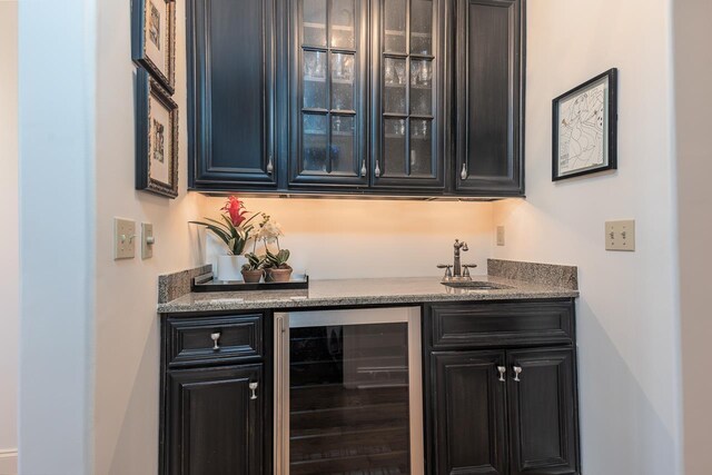 bar featuring stone counters, sink, and beverage cooler