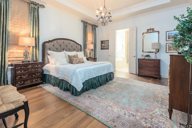 bedroom with ensuite bath, a raised ceiling, crown molding, wood-type flooring, and an inviting chandelier