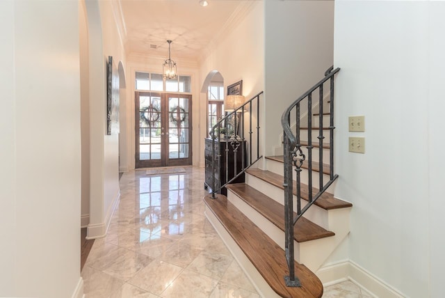 foyer with an inviting chandelier, crown molding, and french doors