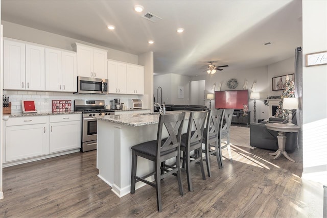 kitchen featuring backsplash, white cabinetry, a kitchen island with sink, appliances with stainless steel finishes, and dark wood-type flooring