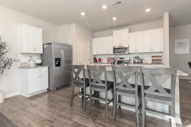 kitchen with white cabinetry, appliances with stainless steel finishes, backsplash, a kitchen island with sink, and light stone countertops