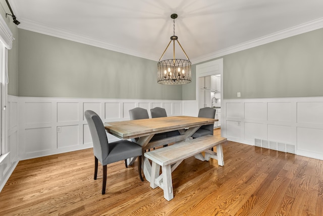 dining space with light hardwood / wood-style floors, ornamental molding, and a chandelier