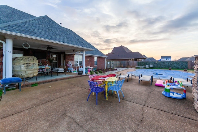 patio terrace at dusk with ceiling fan and a covered pool